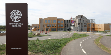 Ravnbakkeskolens skilt med skolen i baggrund