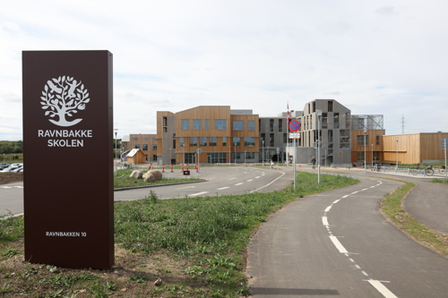Ravnbakkeskolens skilt med skolen i baggrund